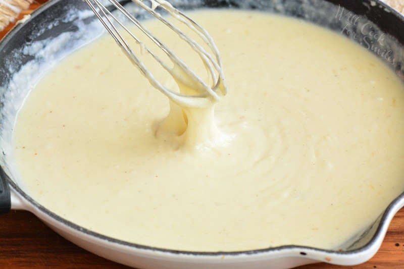 pulling whisk out of the cheese sauce in the pan