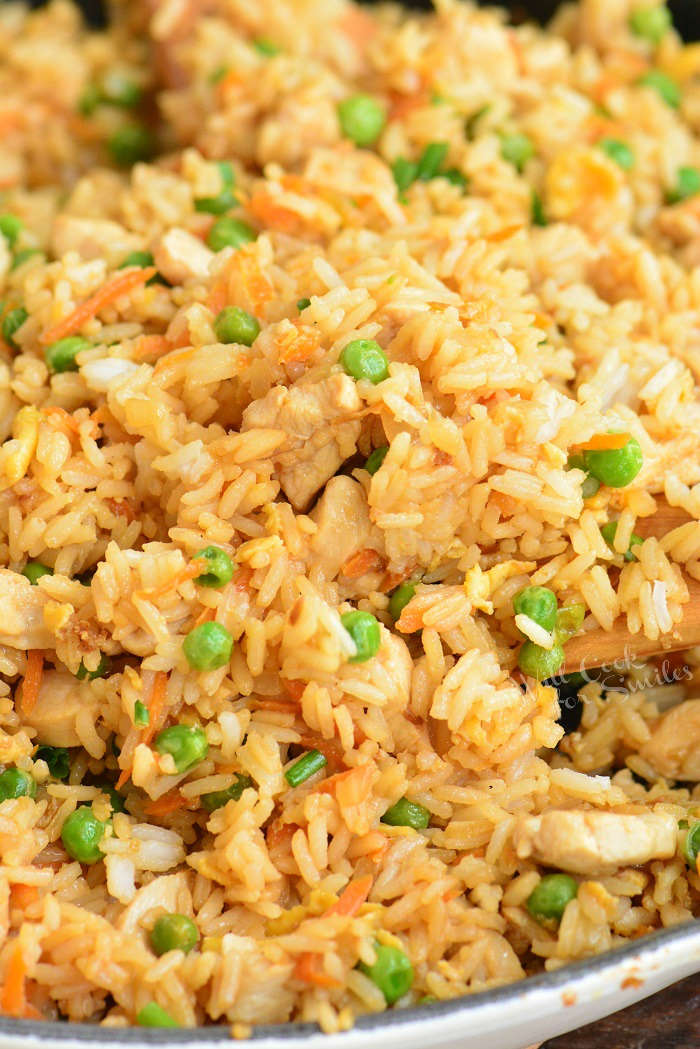 starting to scoop cooked chicken fried rice from the pan with a wooden spoon