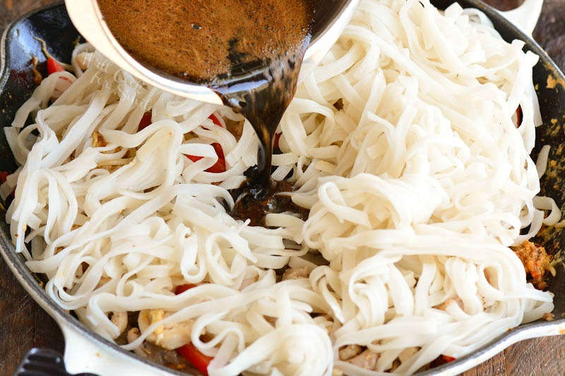 pouring sauce into the pan with noodles and vegetables