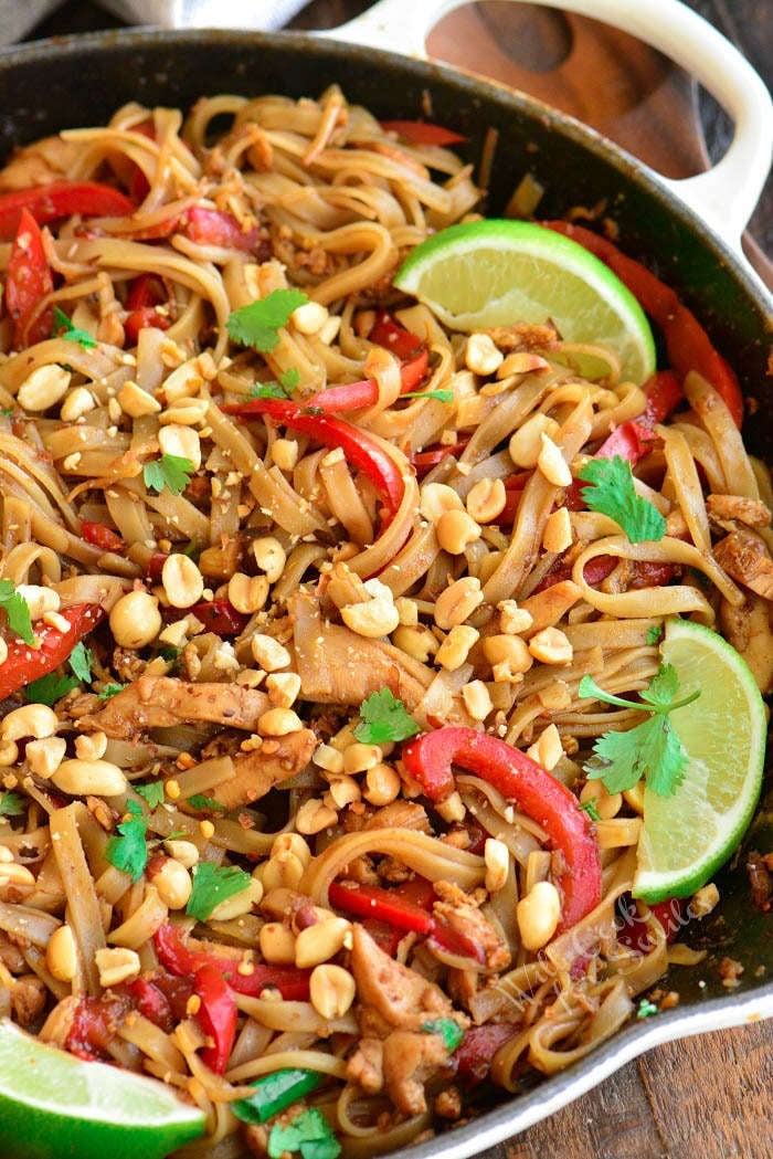 close up of cooked pad thai in a pan topped with peanuts and lime wedges