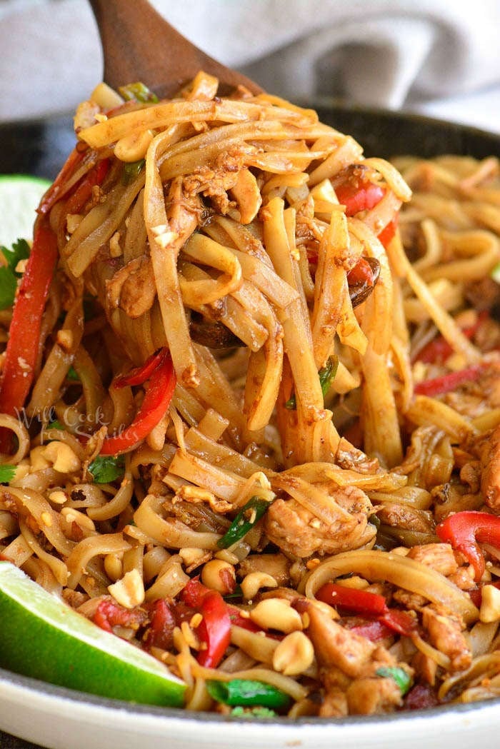 scooping cooked rice noodles with sauce and veggies using a wooden spoon