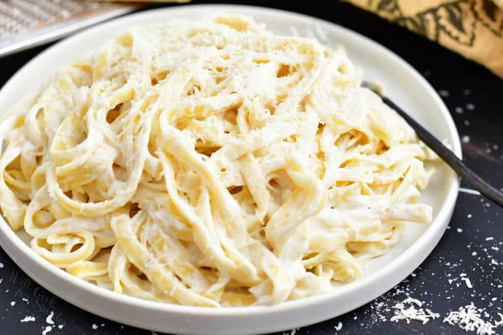 fettuccine alfredo in a white dish with parmesan cheese. 