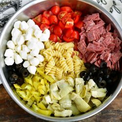 ingredients for antipasto pasta salad laid side by side in a mixing bowl