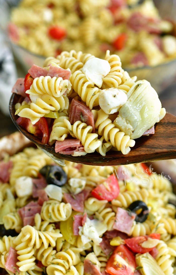 spoonful of mixed pasta salad with pasta, artichoke, salami, mozzarella, and tomato and bowl 