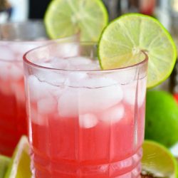 front of glass filled with bright pink cocktail and ice with lime slice on the rim