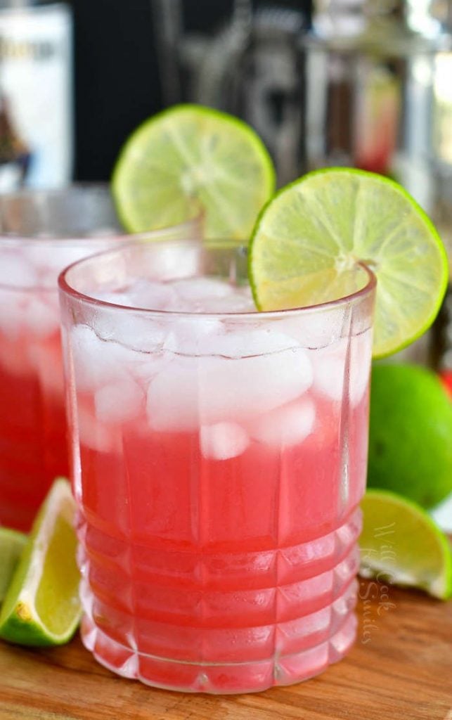 front of glass filled with bright pink cocktail and ice with lime slice on the rim