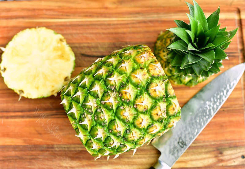pineapple laying on the board with top and bottom cut off next to it and a knife