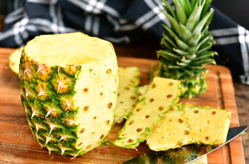 pineapple standing on the board with part of the skin cut off and cut off parts behind it