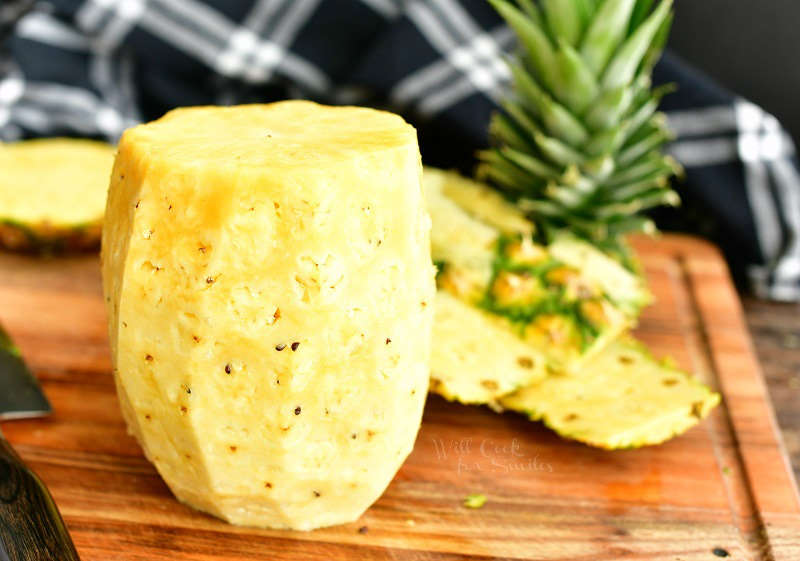 pineapple without the top, bottom, and skin on the cutting board with cut-off pieces behind