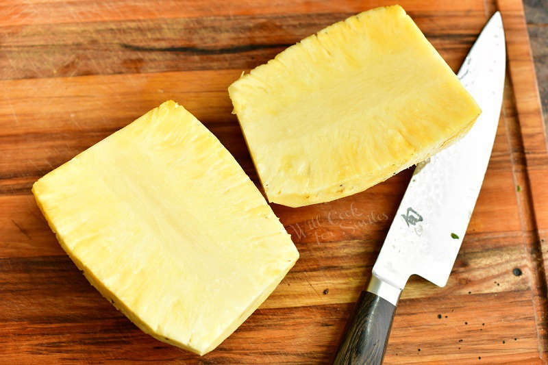 pineapple halves without the skin on the board with a knife next to it