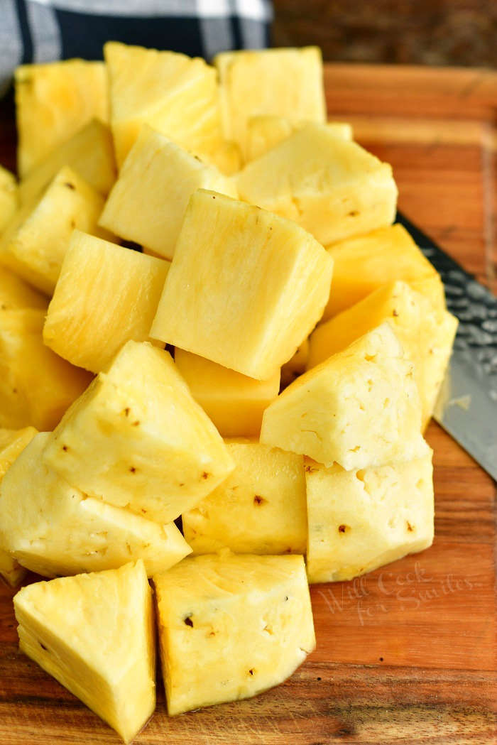 cup fresh pineapple chunks on a cutting board with part of a knife visible