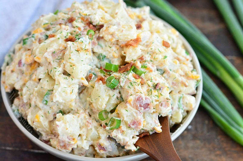 horizontal view scooping potato salad with a wooden spoon from a bowl