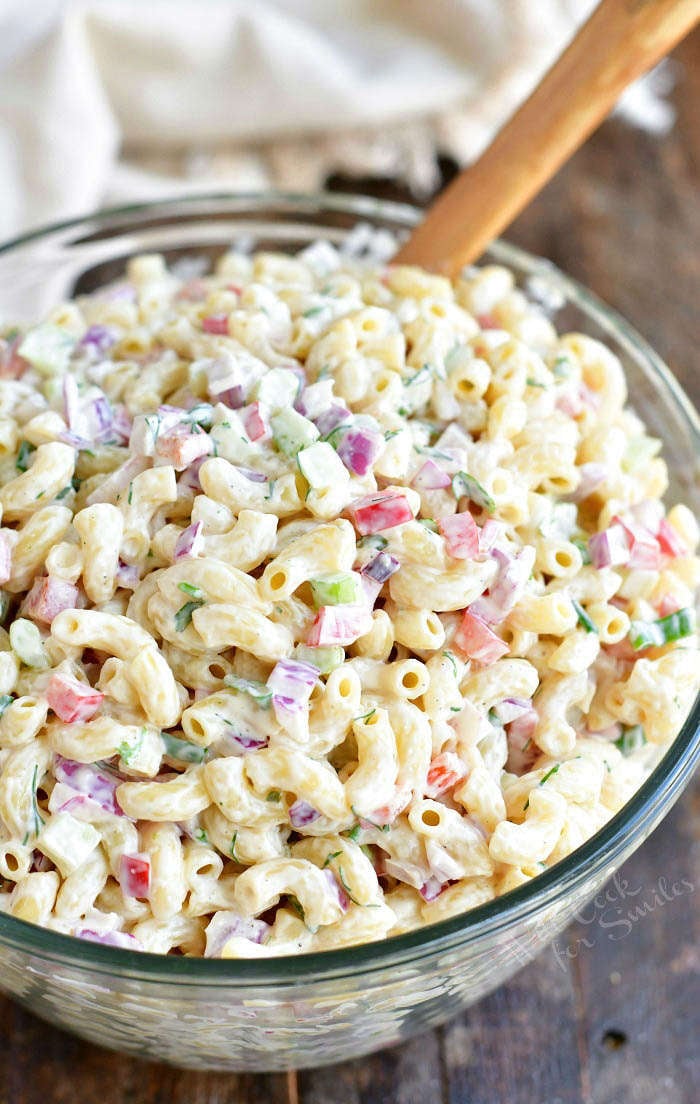 top view of prepared creamy macaroni salad in a glass bowl with wooden spoon spicking out