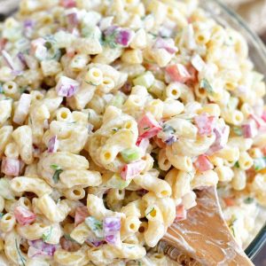 scooping prepared macaroni salad with a wooden spoon