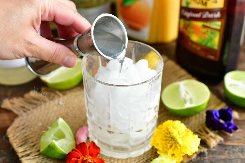 pouring in orgeat syrup into the glass with crushed ice out of a silver measuring cup