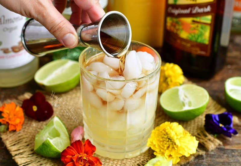 pouring dark rum out of a silver measuring cup into the cocktail glass