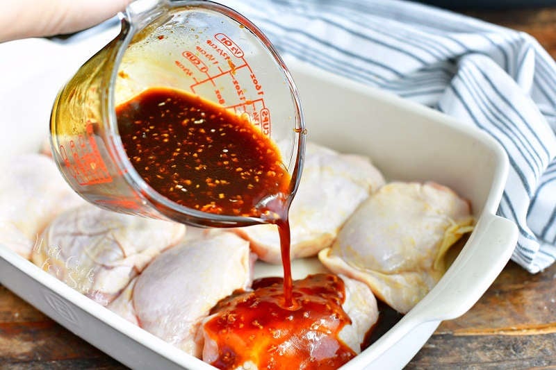 pouring asian sauce over the uncooked chicken thighs in a white baking dish