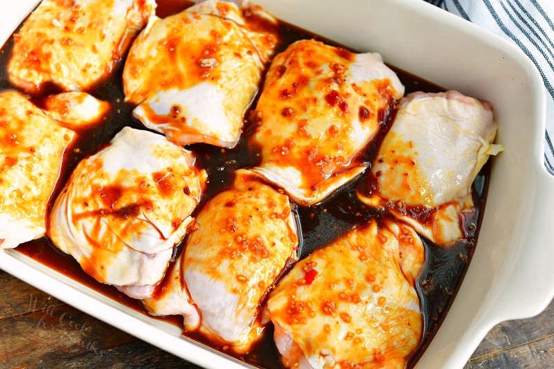 uncooked chicken thighs covered with dark brown sauce in a white baking dish