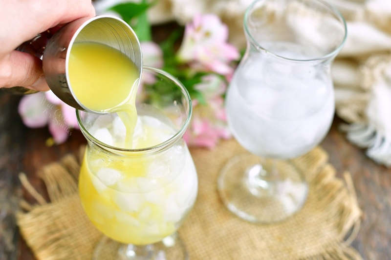 pouring ogange juice from a silver jigger into a glass with ice