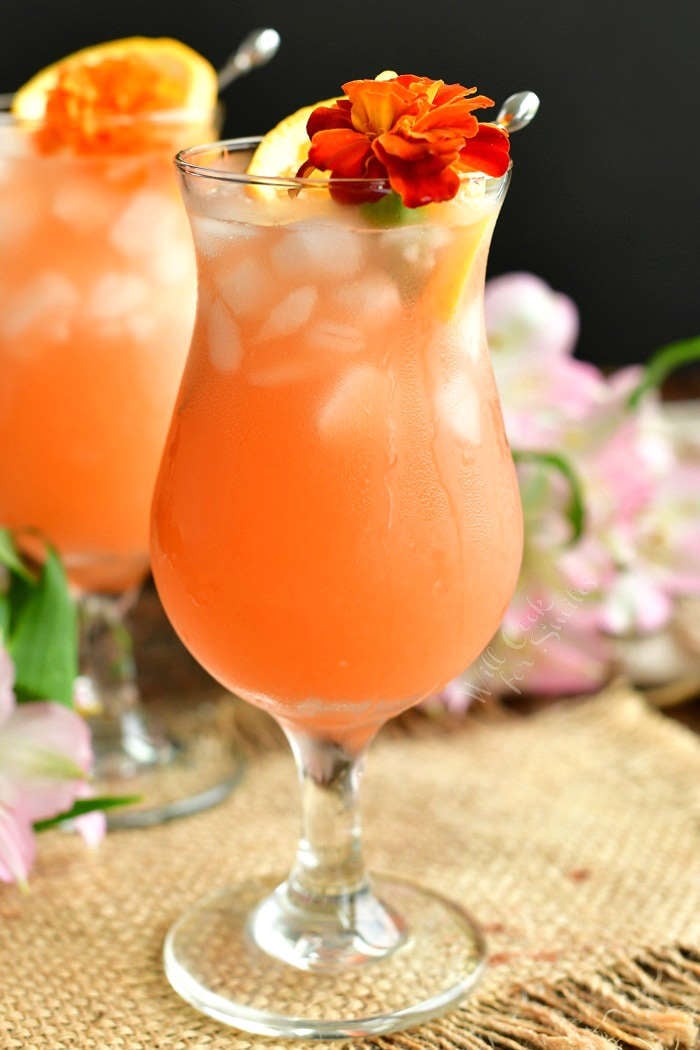 tall curvy glass with peach colored drink decorated with an orange flower and orange