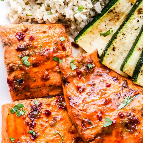 three pieces of salmon on a plate with rice and zucchini slices