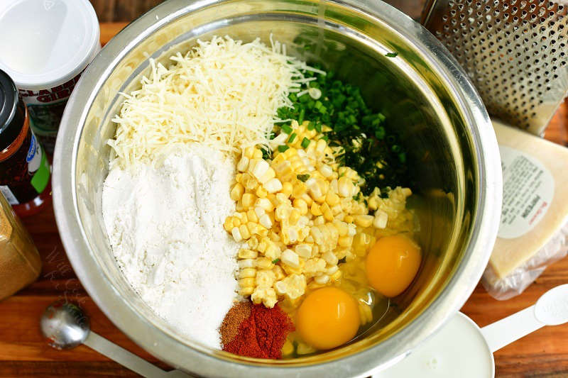 ingredients for the corn mixture side by side inside a mixing bowl and surrounding the bowl on the cutting board