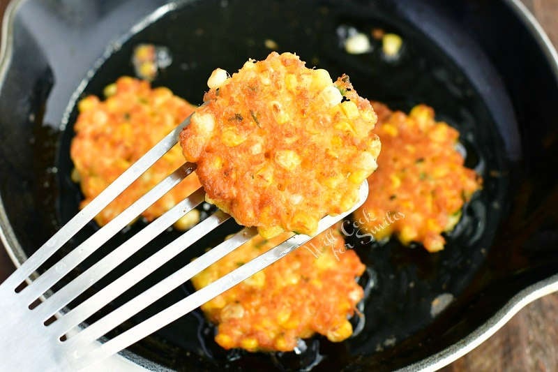 one fritter on a metal fish spatula and fritters in the pan on the background