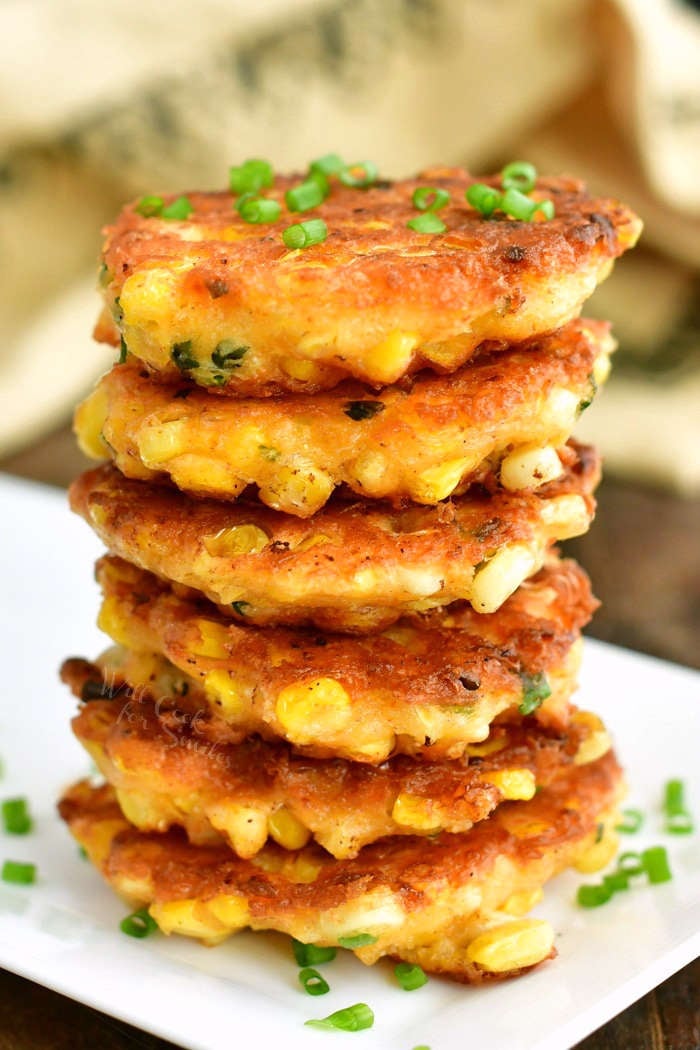 stacked corn fritters on a white plate with chives sprinkled on top