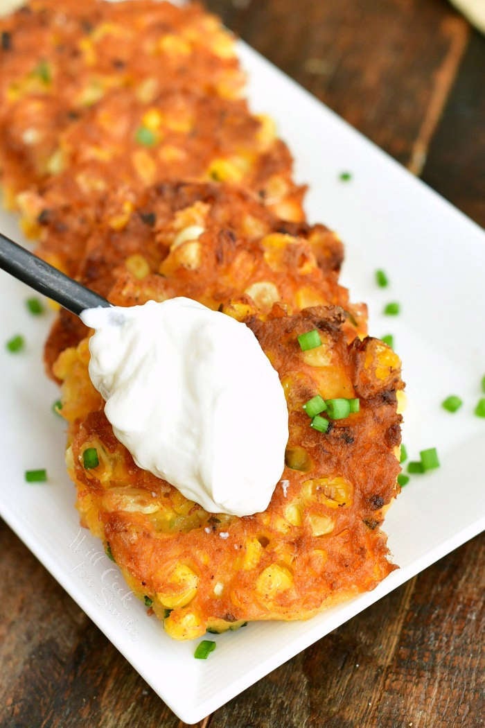 topping cooked fritters with a spoonful of sour cream on a white plate