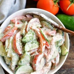 top view of tomato salad mixed in a white bowl with tomatoes on a vine and cucumber next to the bowl