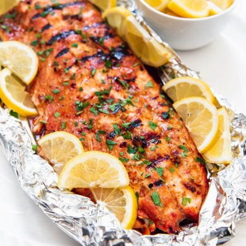 large piece of salmon in foil with lemon slices around it and a small bowl of lemons