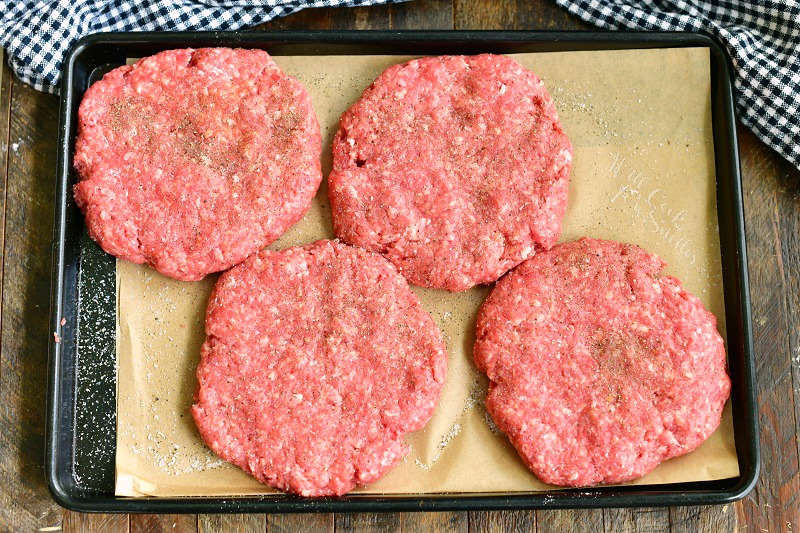 four shaped burger patties uncooked on a black tray