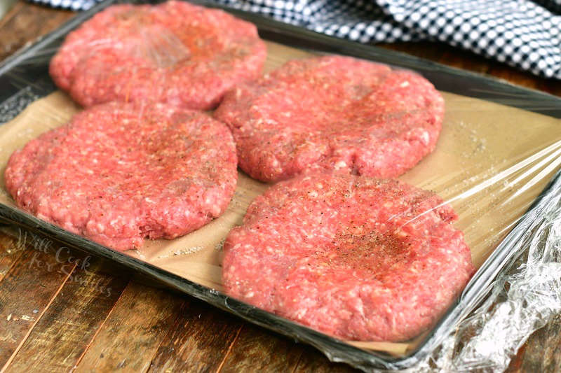 four burger patties uncooked with plastic wrap over it and a thumb print in the middle
