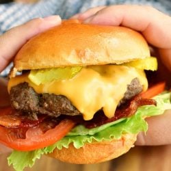 closeup of holding a cheeseburger with two hands and a towel on the background