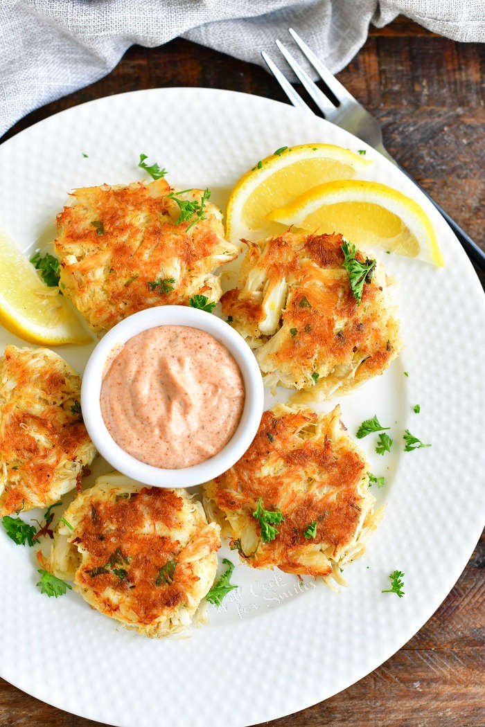 top view of fide crab cakes in a circle and remoulade sauce in the center and lemon wedges on the white plate