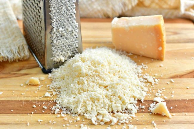 finely grated hard cheese in a mount in the cutting board with box grater and a block of cheese next to it