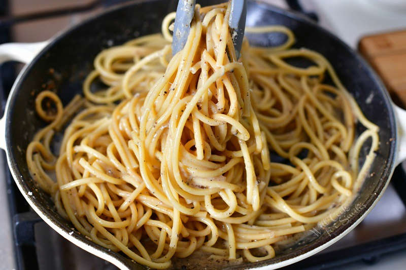 pulling out cheesy pasta from a cooking pan using tongues