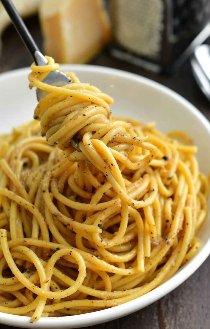 cheesy long pasta swirled onto the fork pulling out of the white bowl with pasta