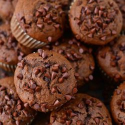 close up of chocolate muffins topped with mini chocolate chips on top of one another and some bananas on the background