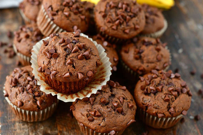 horizontal view of chocolate muffins and one on top with paper liner pulled off