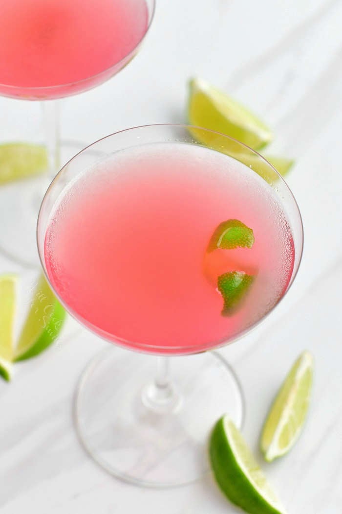 view from the top of the martini glass with light pink cocktail in it and a lime zest floating in the cocktail