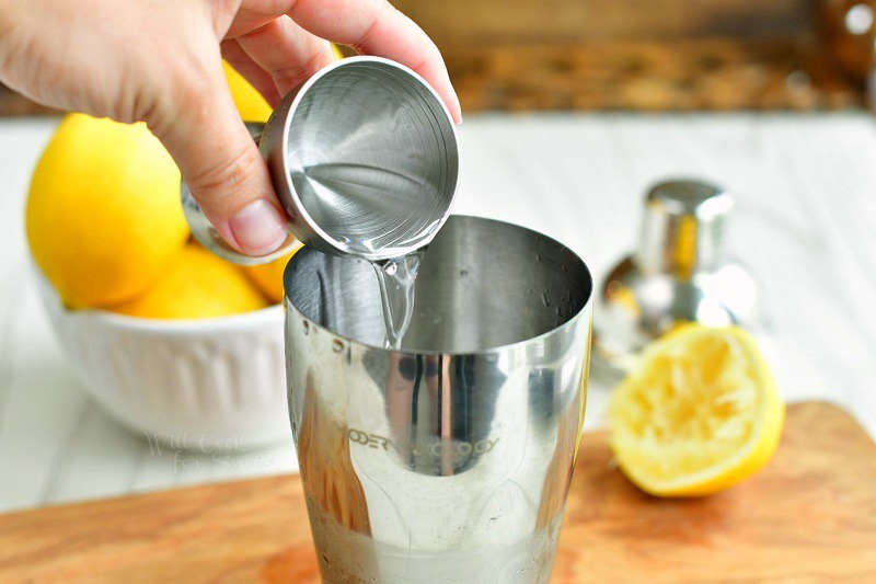 pouring clear liquid out a silver jigger into the cocktail shaker