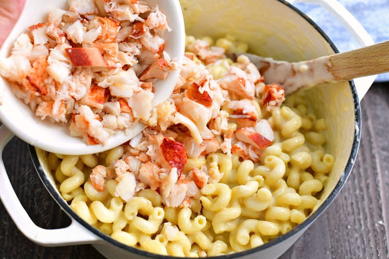 adding cooked lobster meat out of the white bowl into the pot with corkscrew pasta mixed with cheese sauce
