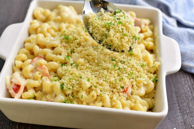 spreading Panko bread crumb topping over the mac and cheese in the baking pan using a silver spoon
