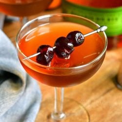closer view of the light brown Manhattan cocktail in a glass topped with dark cocktail cherries on a silver pick