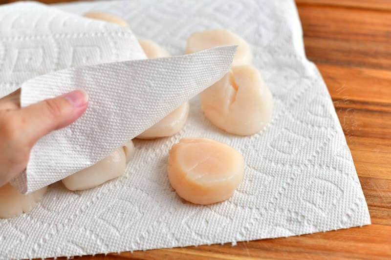 raw scallops on a paper towel and drying each scallop with another paper towel