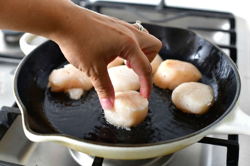 placing a scallop into a hot oiled skillet with a few scallops already in a skillet