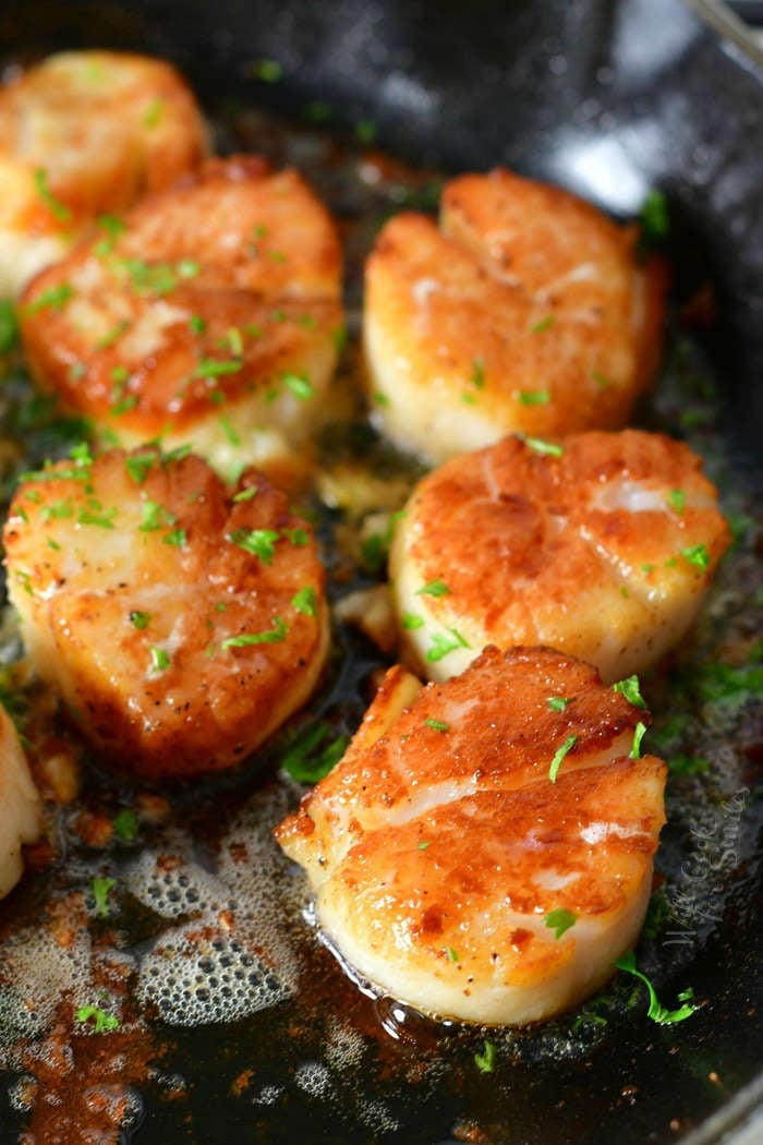 closer view of seared scallops in a skillet with some parsley sprinkled on top