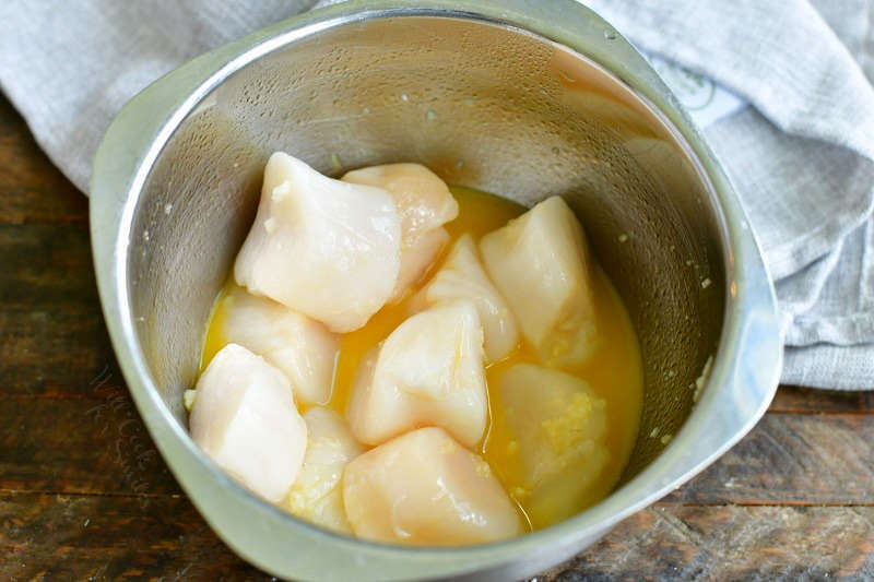 scallops in a metal mixing bowl tossed in butter and garlic mixture