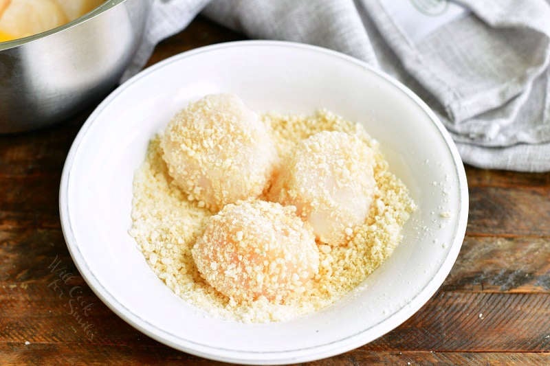 three scallops coated in Panko mix in a white bowl with bread crumbs